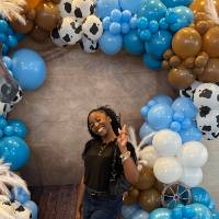 Woman posing in front of balloon arch holding up a peace sign, smiling